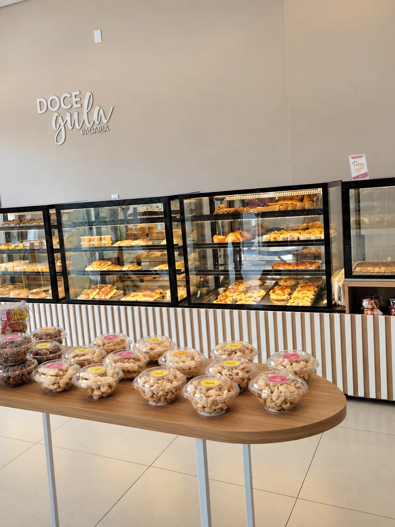 Salão de padaria montado pela Mais Inox, com linha de vitrines refrigeradas iluminadas, balcão de frente ripada e mesa de apoio