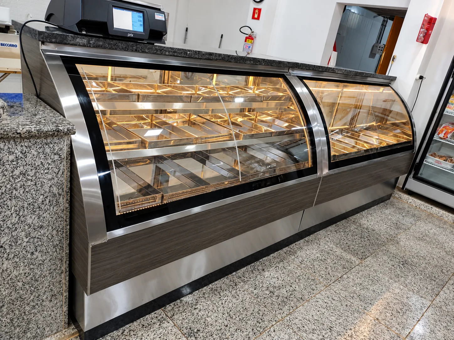 Dois módulos de balcão expositor refrigerado com vidro curvo, perfis em inox, frente em madeira escura, iluminação interna e balança sobre o tampo de granito