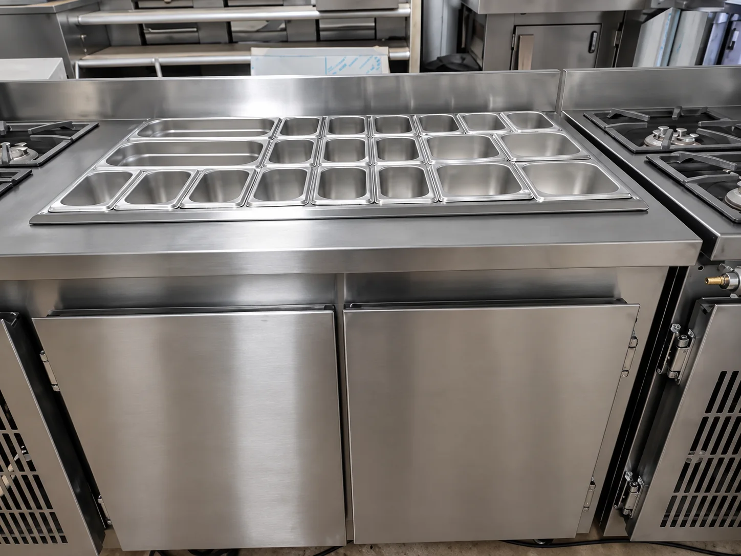 Balcão de preparo em inox com cubas GN no tampo, cooktop lateral e base refrigerada com portas