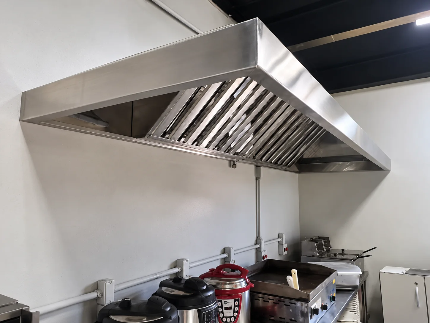 Coifa em inox instalada sobre o fogão e a chapa, em cozinha já revestida