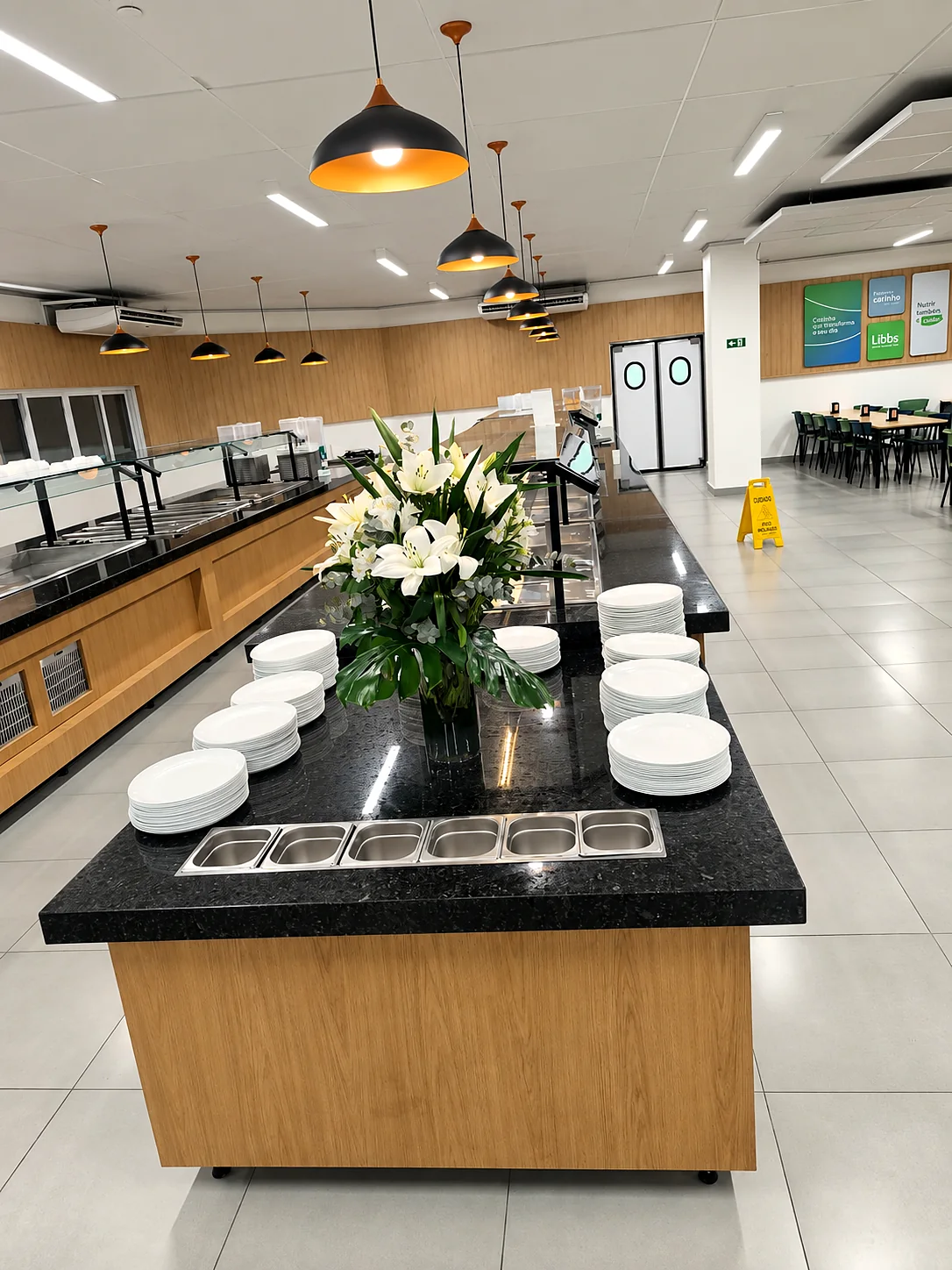Ilha central em inox com tampo de granito, pilhas de pratos e cubas de talheres embutidas