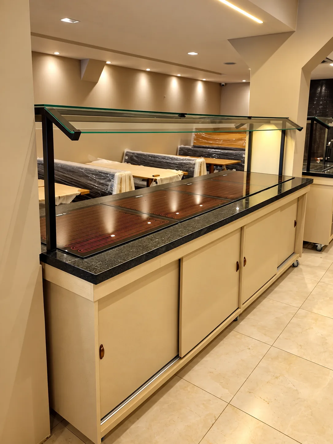 Buffet com placas aquecidas embutidas no tampo de granito, protetor de vidro com estrutura preta e portas de correr na cor do ambiente