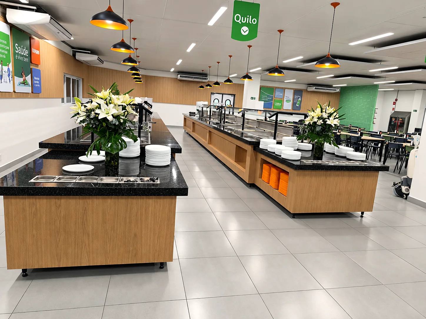 Refeitório com duas linhas de buffet em inox, ilhas centrais de apoio, tampo de granito e luminárias pendentes