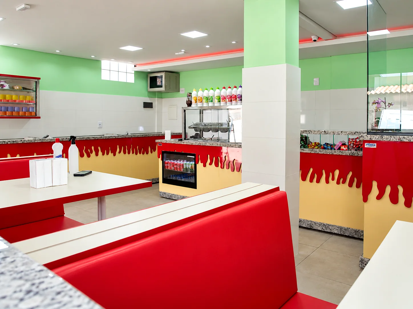 Salão interno de loja de açaí com bancos estofados vermelhos, balcão de atendimento e frigobar embutido
