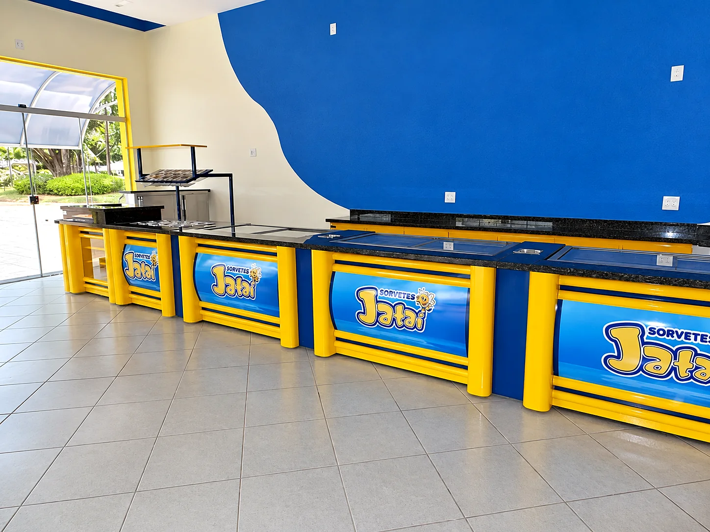 Linha de balcões de sorveteria com frente amarela e azul personalizada, tampo de granito e vitrine refrigerada