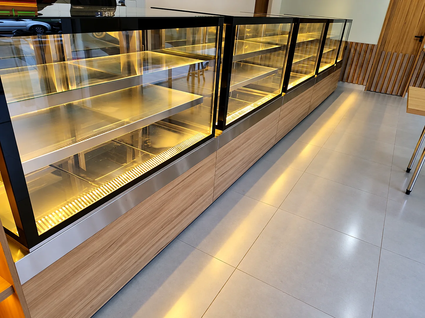 Linha de vitrines refrigeradas vazias com prateleiras de vidro iluminadas e base revestida em madeira