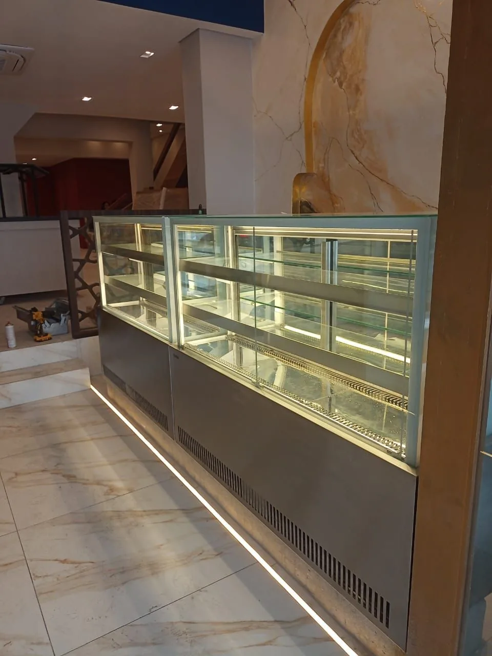 Vitrines refrigeradas com vidro reto e prateleiras iluminadas, base em inox com ventilação frontal e fita de LED no rodapé sobre piso de mármore
