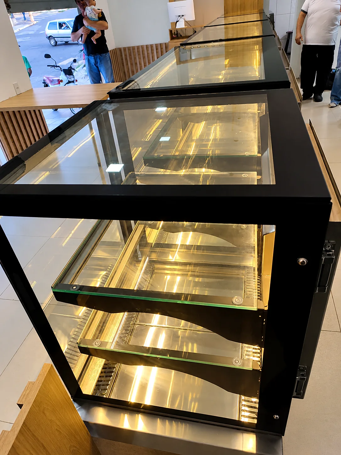 Detalhe de vitrine refrigerada com estrutura preta, prateleiras de vidro e iluminação interna acesa
