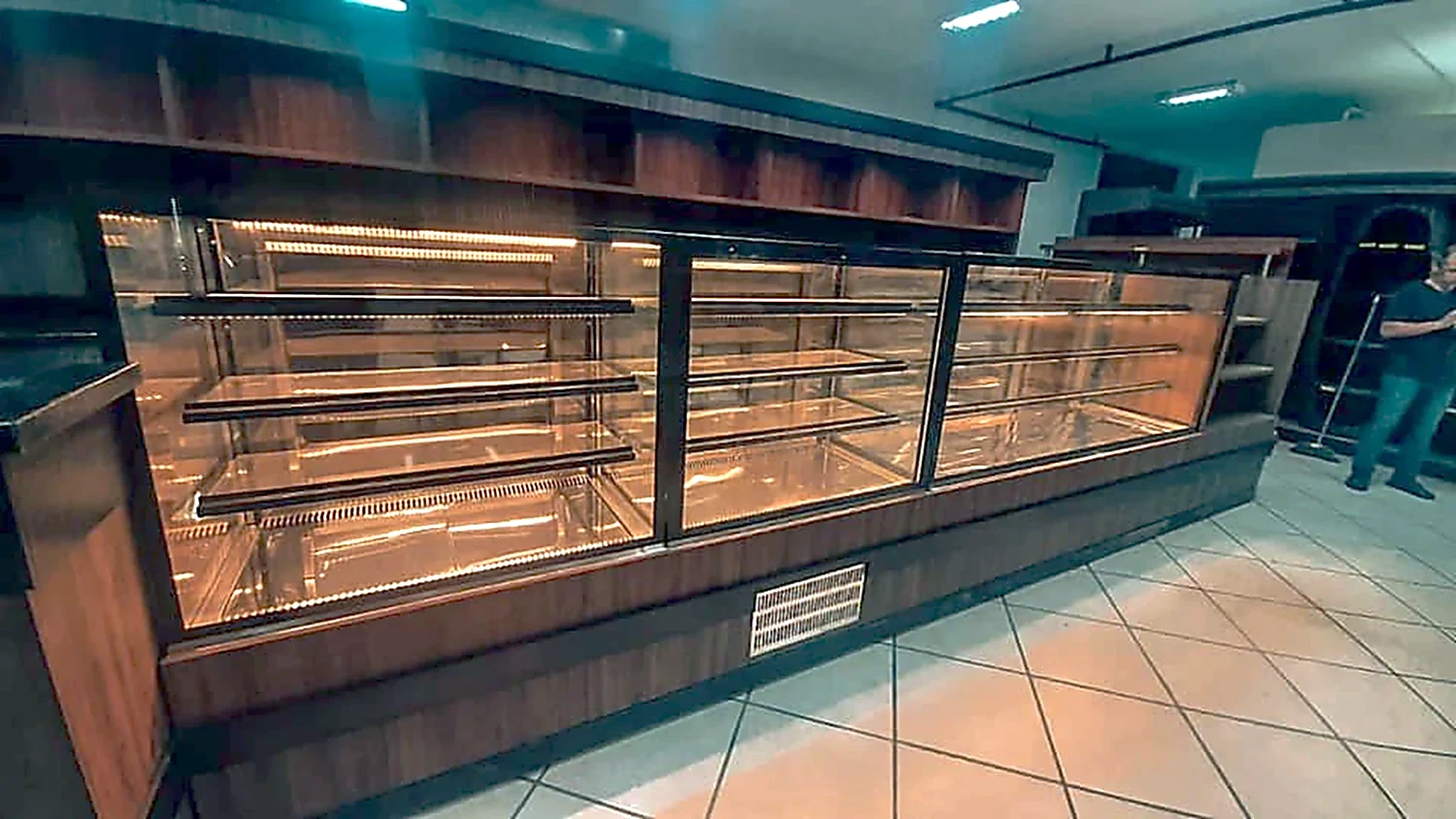 Conjunto de balcões expositores refrigerados em sequência, com estrutura escura e prateleiras internas iluminadas