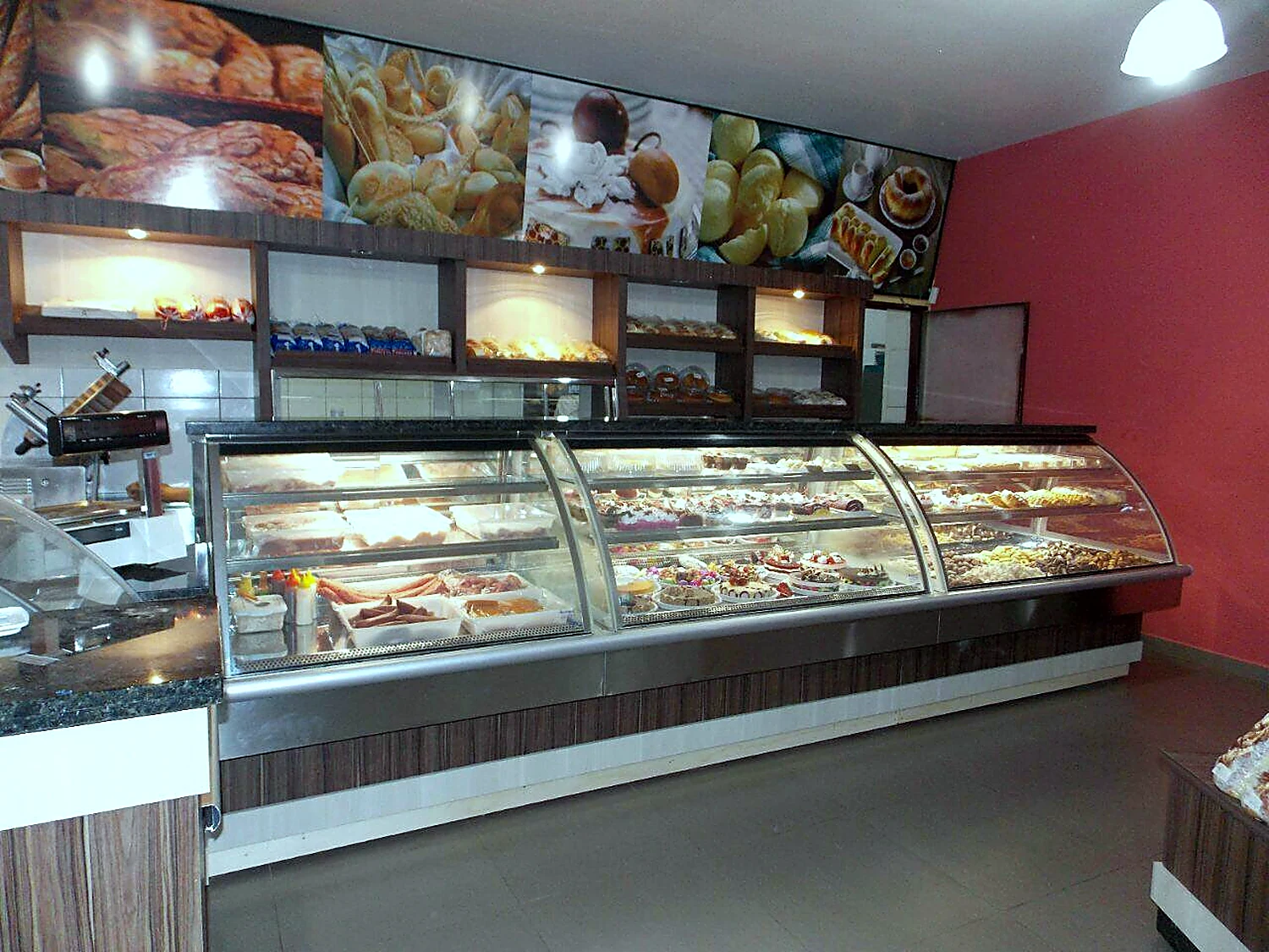 Balcão expositor refrigerado com vidro curvo e prateleiras cheias de salgados e doces